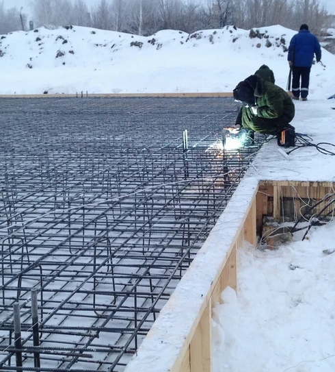 Крупный план арматурного каркаса в опалубке, припорошенного инеем на зимней стройплощадке
