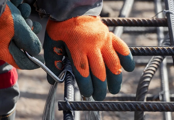 Рабочие руки в перчатках вяжут арматуру проволокой с помощью крючка на снегу