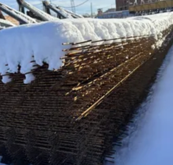 Ржавые арматурные прутья, сваленные на тающем снегу на строительной площадке