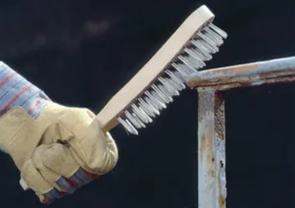 Рука сварщика правильно очищает кромку металла щеткой перед началом сварки электродом МР-3