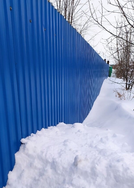 Профнастил для забора зимой с налипшим снегом и сосульками на краях
