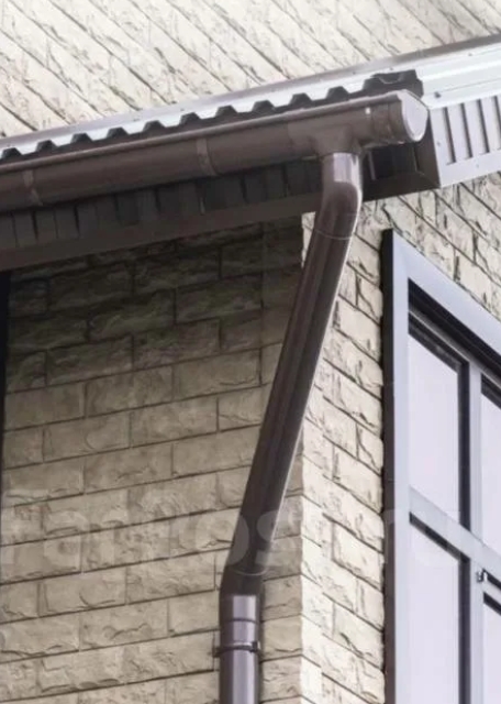 Водосточный желоб на карнизе дома ранней весной во время таяния снега